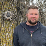 Owen Orsak stands in a forest.