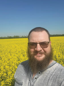 Ryan Gauthier stands in a field of yellow canola flowers.