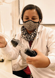 Sharavari Kulkarni in laboratory gear holding an instrument with beetles inside.