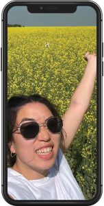 A mockup of a cellphone with Emma posing in front of a canola field in full bloom.