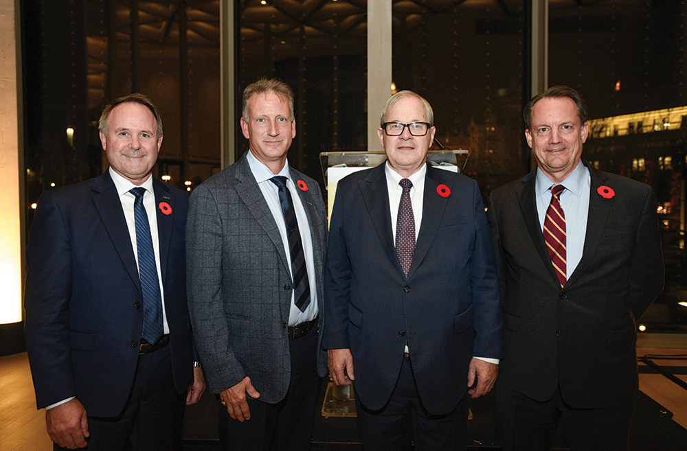 Four men in suits smile for the photo in a lobby.